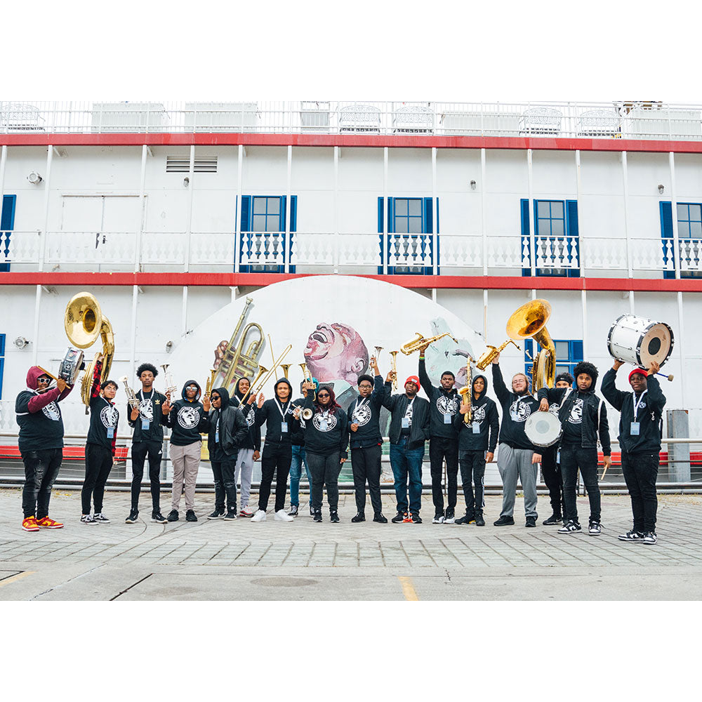 Group of people with musical instruments in front of a large ship.